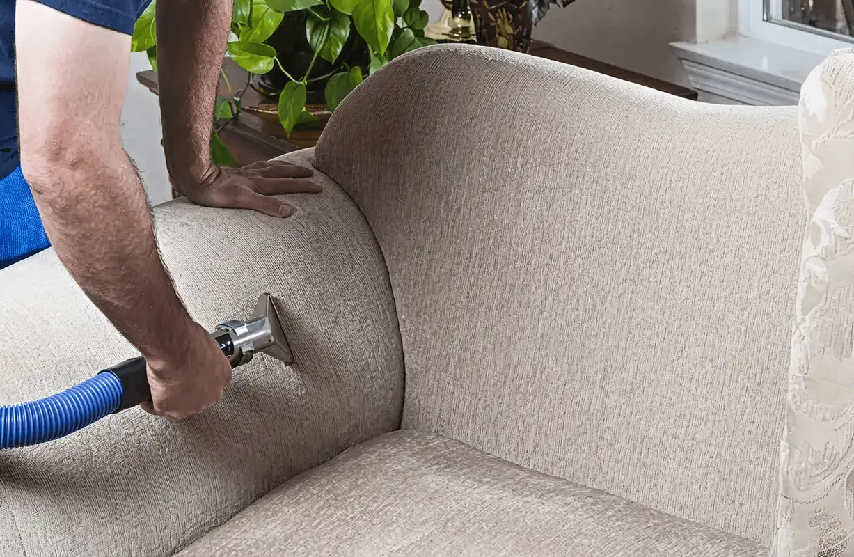 Professional upholstery cleaner deep-cleaning a fabric sofa with a handheld extraction tool and hose, Austin, TX.